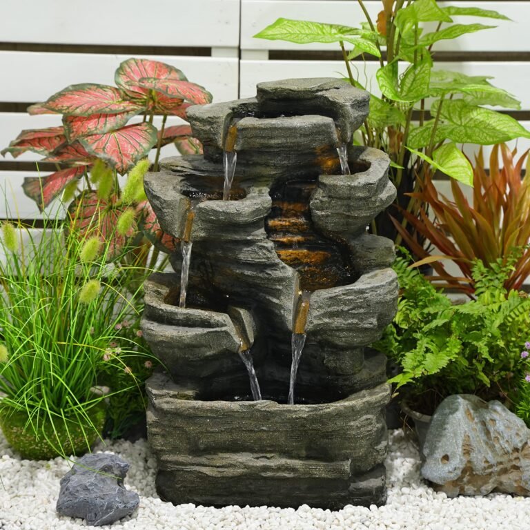 Stone water fountain with cascading water surrounded by plants and white pebbles